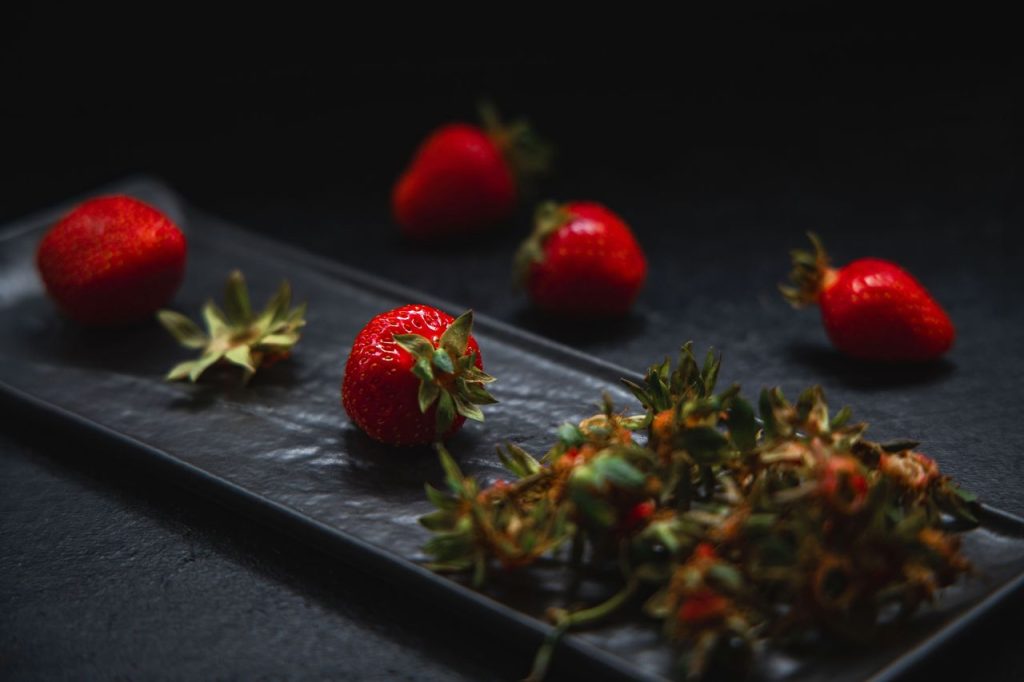 Close-up of ripe red strawberries on a black surface, creating a dramatic, moody scene.